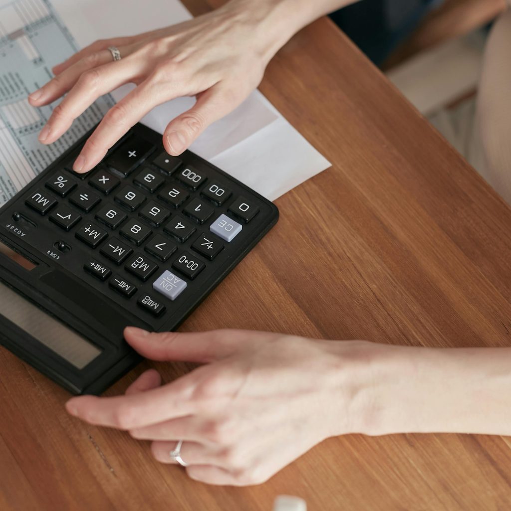 Close-up, a person's hands use a black calculator with a value of 552.2 displayed, while reviewing a tax form on a wooden desk.
